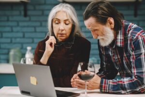 Elderly couple viewing a laptop together, enjoying a quiet moment with wine indoors.